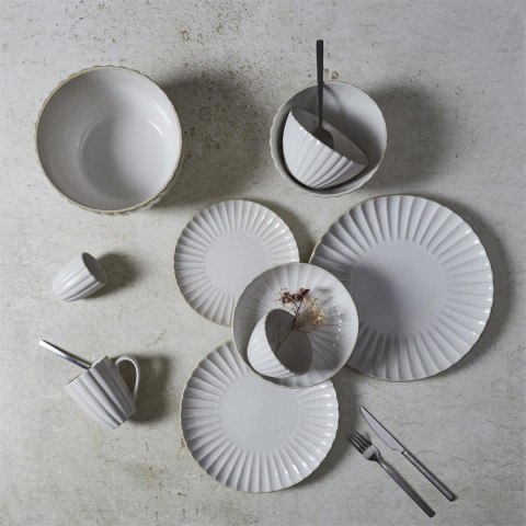 Rozłożona na jasnym stole ryflowana beżowa zastawa ceramiczna z talerzami, kubkami i misami z góry.