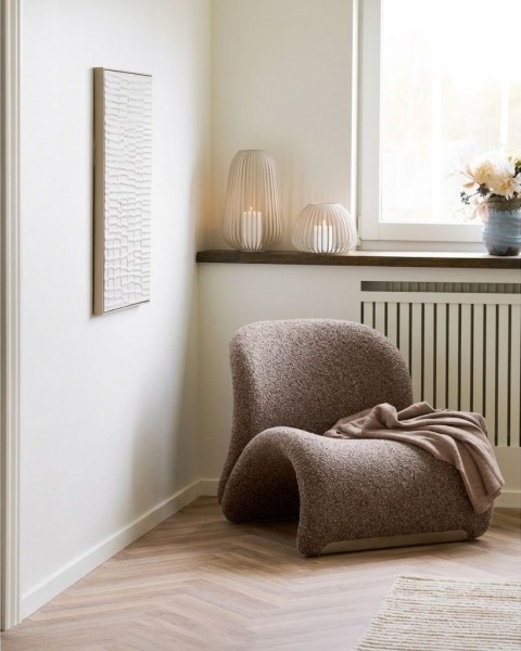 Dekoracyjny koc Attaki Mofu elegancko przewieszony przez zaoblony, brązowy fotel w jasnym pokoju.