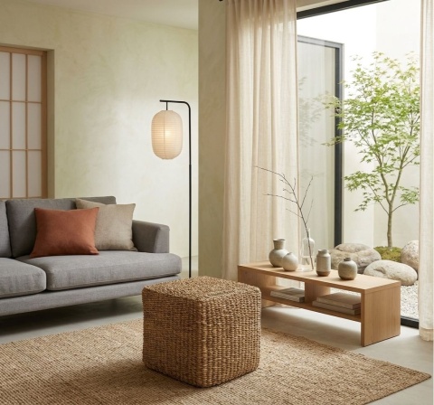 Kwadratowa pufa z trawy morskiej Mittsuami przed szarą kanapą w minimalistycznym salonie japandi.
